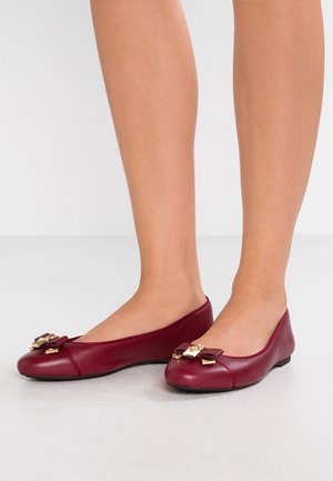 Bordeaux læderballetsko med rund tå, prydet med en sløjfe og guld hardware, på en flad sål. Glat tekstur med minimal syning.