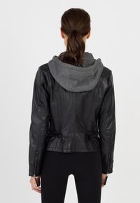 Svart läderjacka med grå huva, utrustad med dragkedjor, sidobälten och texturerade armbågsfickor. Slätt material med figursydd design.