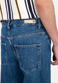 Hellblaue Jeans aus Denim mit hoher Taille, geradem Bein Design und sichtbaren Nähten. Enthält zwei Gesäßtaschen und ein Etikett am Taillenbund.