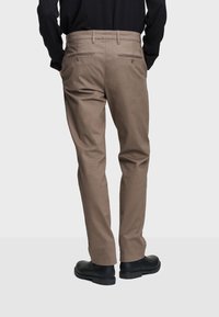 Beige puuvillahousut suoran leikkauksen, näkyvien takataskujen ja sileän pinnan kanssa. Mustat kengät täydentävät asua.