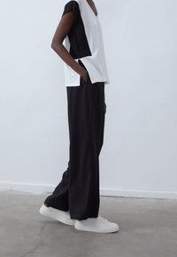 Top bloqueado en blanco y negro con escote en V y mangas cortas, combinado con pantalones negros holgados y zapatillas blancas. Textura de tela suave.