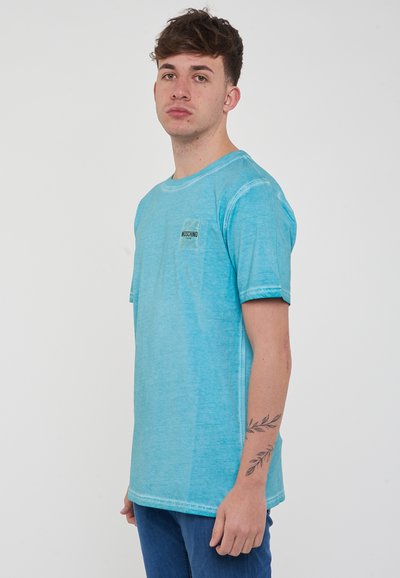 T-shirt in cotone turchese con scollatura a girocollo e maniche corte, dotato di una piccola etichetta nera sul lato sinistro del petto. Tessuto strutturato.