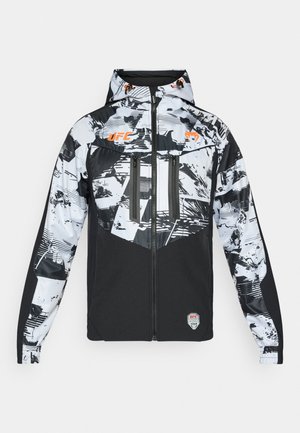Zwart-wit jack met abstract patroon, ritssluiting, twee voorzakken, capuchon met oranje accenten en UFC-logo op de borst.