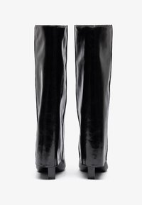 Mustad nahk-knee kõrgused saapad mustas lakkseidmes, sujuva tekstuuriga, ruudukujuliste kontsadega ja sujuva disainiga. Tagantvaade toob esile kõrge varre.