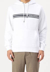 Felpa bianca con cappuccio e tasca frontale, caratterizzata da strisce orizzontali nere e dettaglio logo sul petto. Morbido materiale in cotone.