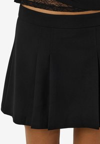 Črna plisejska krila z gladko teksturo, ki ima širok pas in rob, ki se končuje nad sredino stegna. Klasična zasnova, brez vzorcev.