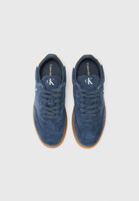 Plave suede tenisice s okruglim vrhom, kremastim akcentima na ovratniku i gumenim potplatom. Imaju vezanje s čipkastom i logo sa strane.