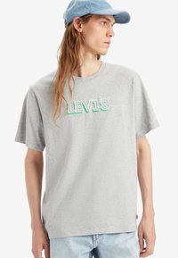 Camiseta de algodón gris con cuello redondo, mangas cortas y el logo "LEVI'S" en letras verdes y blancas en el pecho. Corte casual.