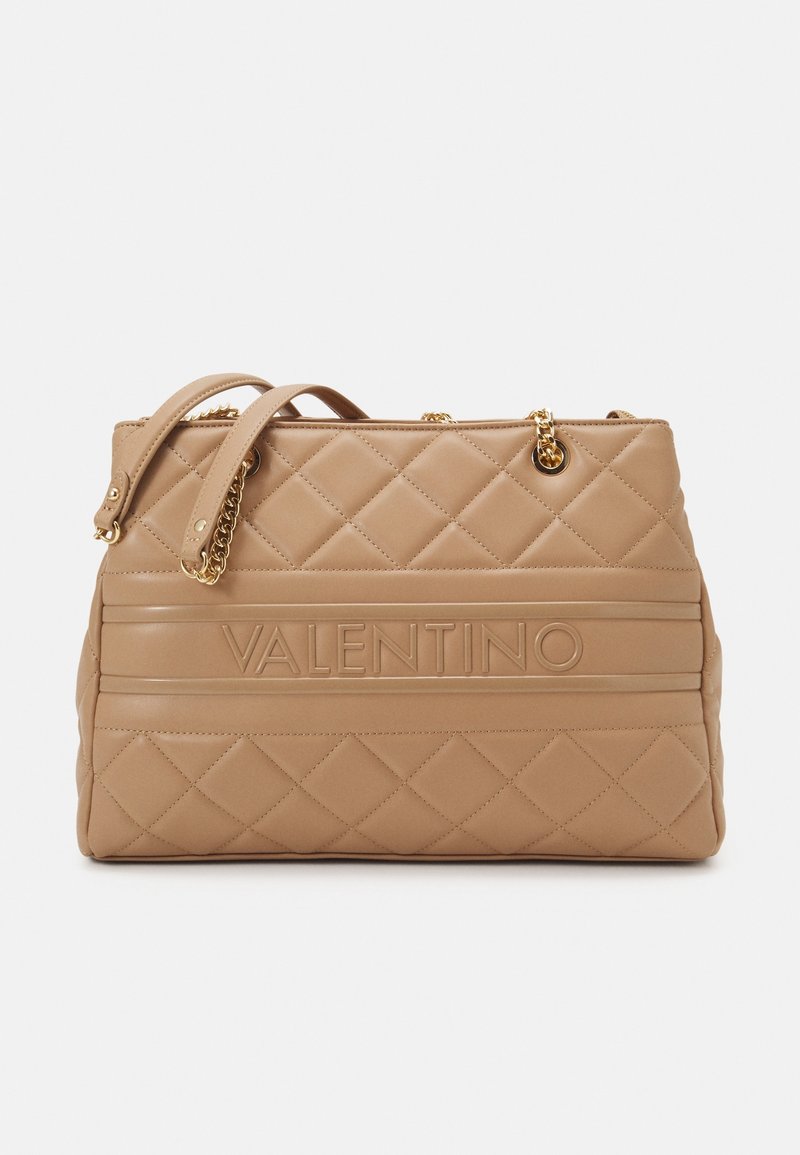 Prošívaná béžová kožená kabelka se zlatými řetízkovými akcenty a embosovaným logem "VALENTINO". Obsahuje dvě krátké rukojeti pro nošení.