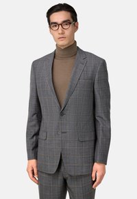 Traje de cuadros gris con una chaqueta estructurada, solapas muescas y dos botones. Llevado sobre un cuello de tortuga beige. Ajuste slim y textura suave.