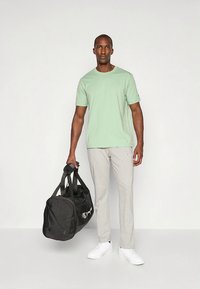 Svijetlozelena majica kratkih rukava, sive trenirka hlače, bijele tenisice i crna sportska torba. Minimalistički dizajn s opuštenim krojem.