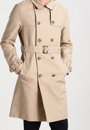 Beige trench coat vyrobený z jemné látky, s dvojitým zapínáním na knoflíky, opaskem v pase a knoflíkovými manžetami.