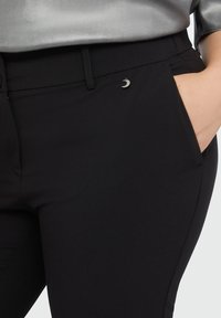 Black trousers made from a stretch fabric, featuring a sleek design, pocket details, and a small silver accent on the waistband.