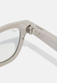 Close-up of beige Ray-Ban Meta smart glasses hinge with metal joint and infinity symbol on the arm.