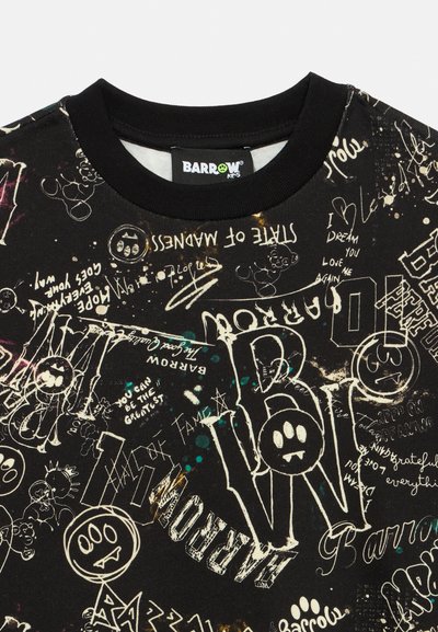 Camisa de manga corta negra con diseños de texto mixtos en blanco, amarillo y verde, que presenta diversas gráficas expresivas y un cuello redondo.