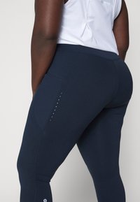 Leggings de color navy con una textura suave, que cuentan con costuras diagonales y puntos reflectantes decorativos a lo largo del lateral. La tela tiene un ajuste elástico.
