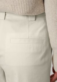 Cremfarbene Hose mit einer flachen Gesäßtasche. Das Material scheint Baumwolle mit einer glatten Textur zu sein. Pullover in einem hellen Beige mit gestricktem Design.