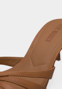 Ταφ δερμάτινο σανδάλι με τακούνι, λεπτά σταυρωτά λουράκια και μαξιλαρωμένο πέλμα, με ανάγλυφο όνομα της μάρκας στην εσωτερική πλευρά της φτέρνας.