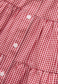 Tessuto a quadretti rossi e bianchi con un design raggrinzito, caratterizzato da bottoni bianchi a forma di fiore e una texture liscia.