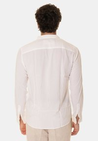 Camicia bianca a maniche lunghe realizzata in tessuto leggero con orlo curvo, polsini abbottonati e una finitura testurizzata discreta.