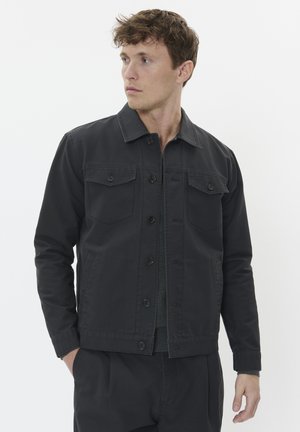 Chaqueta de mezclilla negra con collar en punta, cierre frontal de botones, dos bolsillos en el pecho y un corte relajado. Tejido ligeramente texturizado, diseño casual.