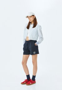 Geknipte, gestreepte overhemden in blauw en wit, gecombineerd met marineblauwe shorts met een logo. Rood sneakers en een witte pet maken de look compleet.