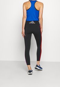 Leggings neri con strisce laterali multicolori, vita elastica con il logo Adidas, abbinati a un top blu e sneaker nere.