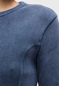 Μπλε μακρυμάνικη μπλούζα με ριμπ ύφανση, στρογγυλή λαιμόκοψη και εμφανείς ραφές. Το υλικό έχει απαλή υφή με διακριτική γυαλάδα.