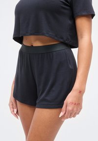 Μαύρο, ριμπ σετ ρούχων για χαλάρωση που περιλαμβάνει cropped τοπ και σορτς με ψηλή μέση και λείο λάστιχο, δίνοντας έμφαση στην άνεση και την ελευθερία κινήσεων.