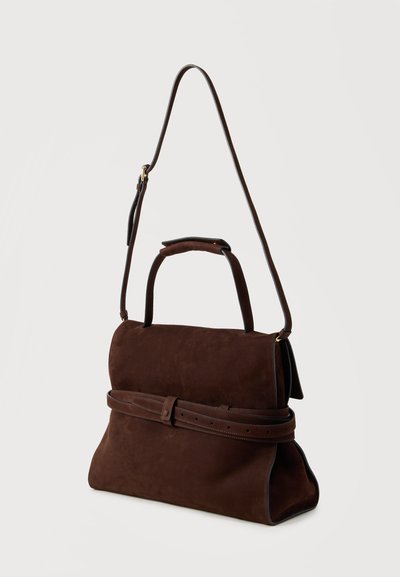 Sac en daim marron foncé avec une poignée supérieure, une longue bandoulière réglable et une ceinture décorative à boucle autour du milieu sur un fond clair.