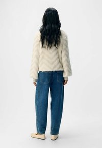 Krämfärgad, fluffig tröja med zigzag-mönster, i kombination med löst sittande blå jeans och ljusa slip-on skor. En enkel bakgrund.