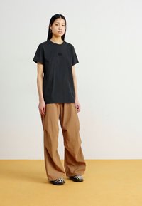 T-shirt en coton noir à manches courtes et encolure ronde, associé à un pantalon marron à coupe décontractée et des chaussures rayées. Couleurs unies, coupe décontractée.