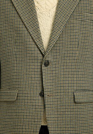Rudas ir mėlynas houndstooth rašto švarkas su dviem priekinėmis kišenėmis, vieno mygtuko uždarymu ir tekstūruotu megztiniu po juo.