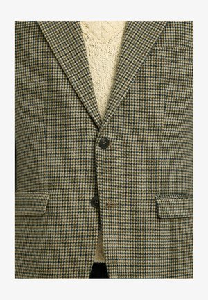 Blazer a scacchi marrone e blu con due tasche frontali, chiusura a un bottone e maglione in maglia testurizzata sotto.