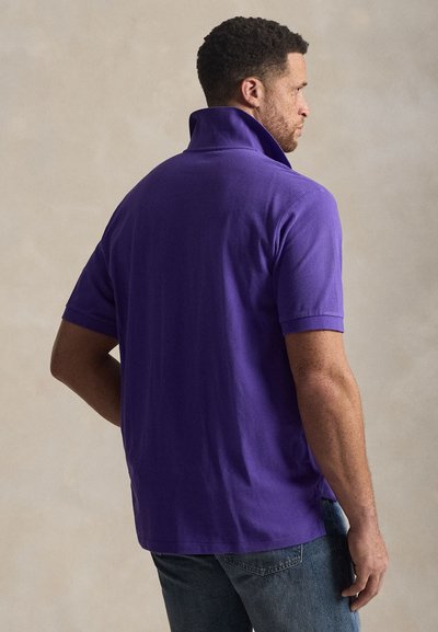 Μωβ μπλουζάκι πόλο με κοντά μανίκια και ανασηκωμένο γιακά. Κατασκευασμένο από υφ ασμάτινη υφή, διαθέτει πλάγιες σχισμές για ευκολία στην κίνηση.