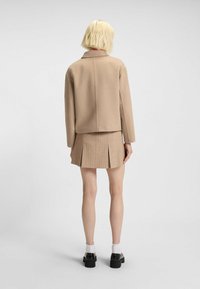 Beige wool jacket with a collar, paired with a beige pleated skirt featuring thin vertical stripes. Model wears black platform shoes and white socks.