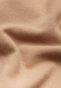 Beżowa faktura tkaniny z subtelnym wzorem kratki, prezentująca miękkie, tkane włókna, które tworzą gładką, matową powierzchnię.