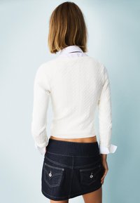 White cable-knit sweater with long sleeves, paired with a dark denim mini skirt featuring back pockets and visible stitching details.