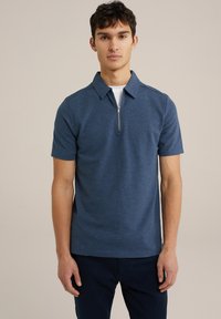 Polo de manga corta en tejido azul oscuro texturizado, con cremallera en el frente y cuello de punta. Llevado sobre una camiseta blanca.
