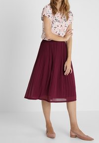 Blusa rosa a maniche corte con fantasia floreale abbinata a una gonna midi plissettata color bordeaux, completata da ballerine rosa chiaro.