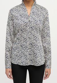 Blouse blanche avec un motif abstrait bleu marine, à manches longues et col montant. Fabriquée en tissu léger, elle dispose d'une fermeture à boutons sur le devant.
