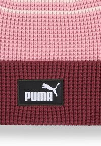 Gebreide muts in tinten roze en bordeauxrood met een geribbelde textuur, voorzien van een zwart rechthoekig Puma-logo etiket met witte opdruk.