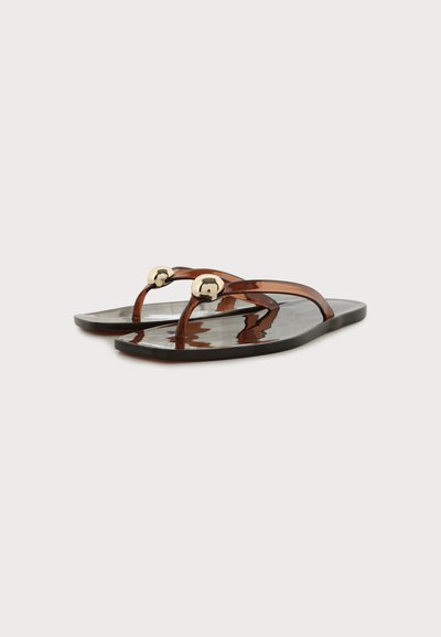 Paire de tongs marron foncé brillantes avec des fines brides et des décorations rondes dorées brillantes sur le dessus, sur un fond clair uni.