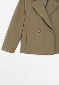 Khakifarbene, doppelt verknöpfte Jacke mit großem Reverskragen, zwei Knöpfen, zwei seitlichen Taschen und strukturierten Ärmeln. Texturiertes, leichtes Material.