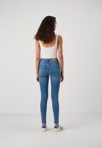 Skinny jeans in a light blue wash with a high waist, featuring back pockets and a leather label. Worn with a white tank top and sneakers.
