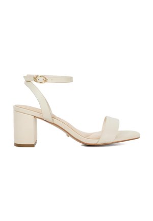 Sandales à talon bloc beiges avec bride de cheville réglable, en cuir lisse, design à bout ouvert et accents minimalistes.