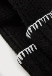 Écharpe noire en tricot avec un tissu texturé et des accents de couture blanche le long des bords, présentant un motif côtelé et une texture douce.
