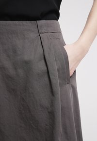 Jupe en tissu gris avec un design plissé, des poches latérales et une texture lisse, complétée par une taille plate.