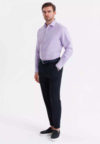 Camisa de botones de color púrpura claro con mangas largas, combinada con pantalones negros ajustados y zapatos negros sin cordones. Tela suave y corte a medida.