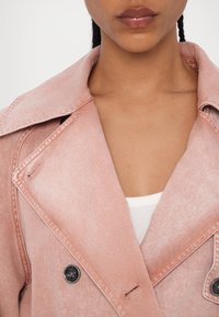 Femme portant une veste en jean rose clair par-dessus un haut blanc côtelé, montrant le col, l’encolure et les lèvres.